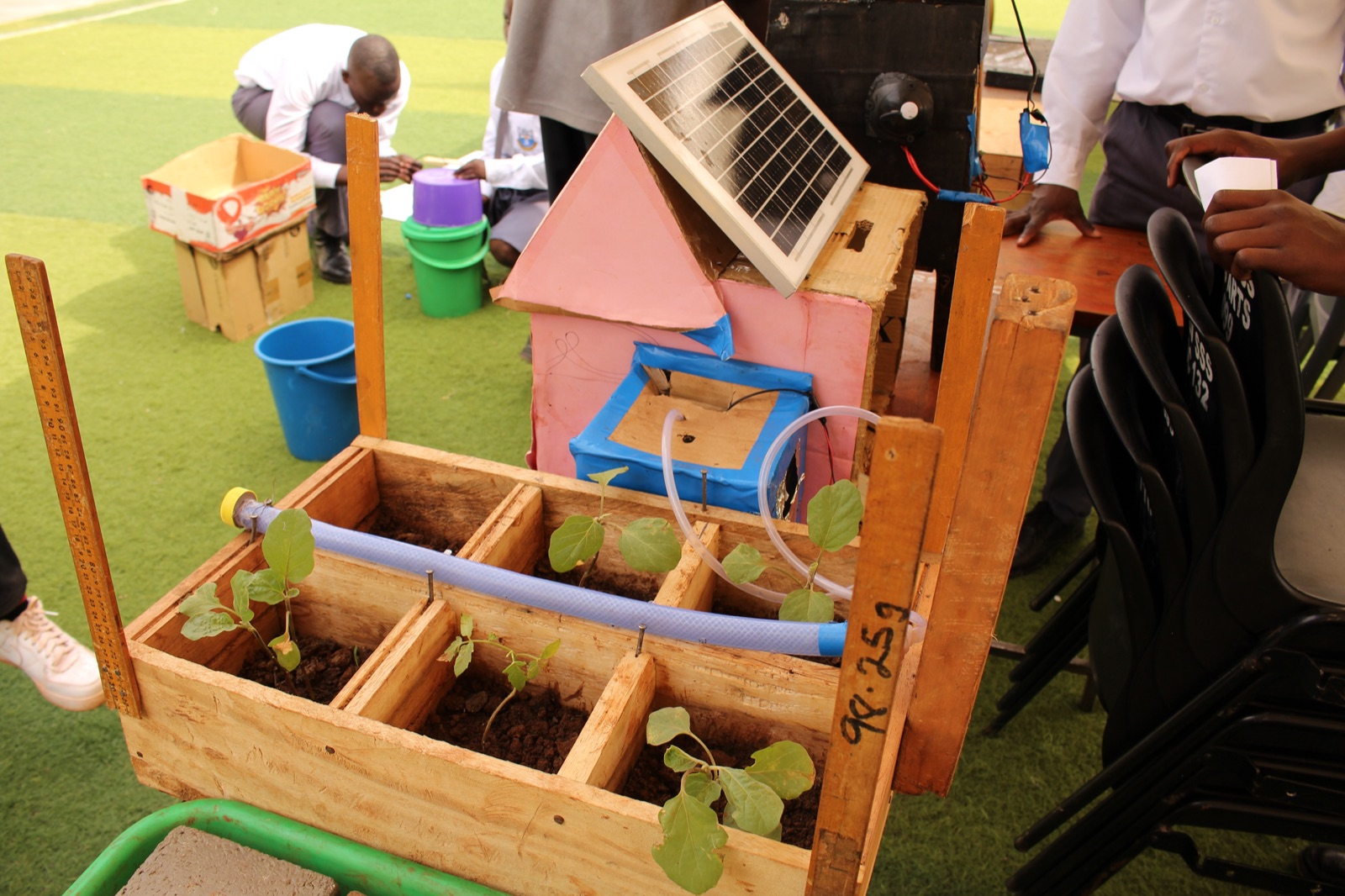 A student-built model of a solar-powered irrigation system, with seedlings in wooden planting boxes