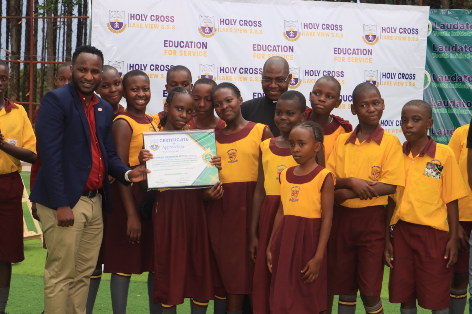 Students holding a certificate of appreciation in front of a Holy Cross Lake View and Laudato Youth Initiative backdrop