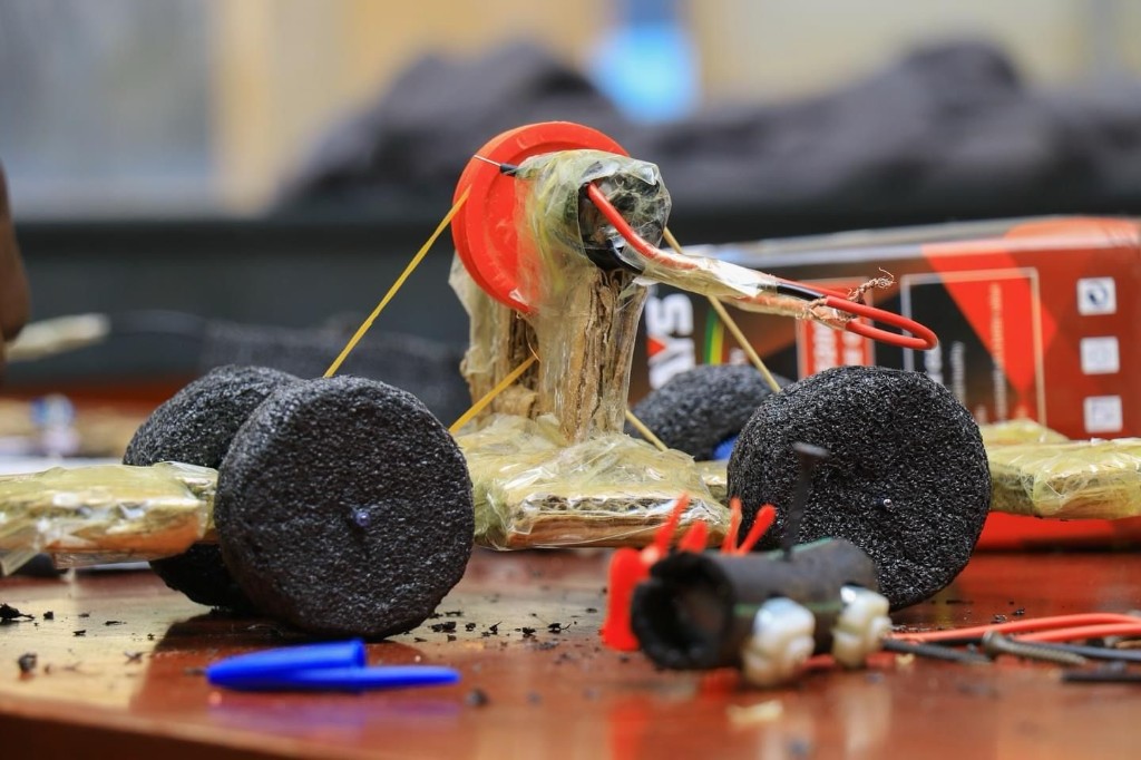 Close-up of a student-made toy car built from cardboard, foam wheels, tape, and a small motor with a belt drive—a hands-on STEM engineering project