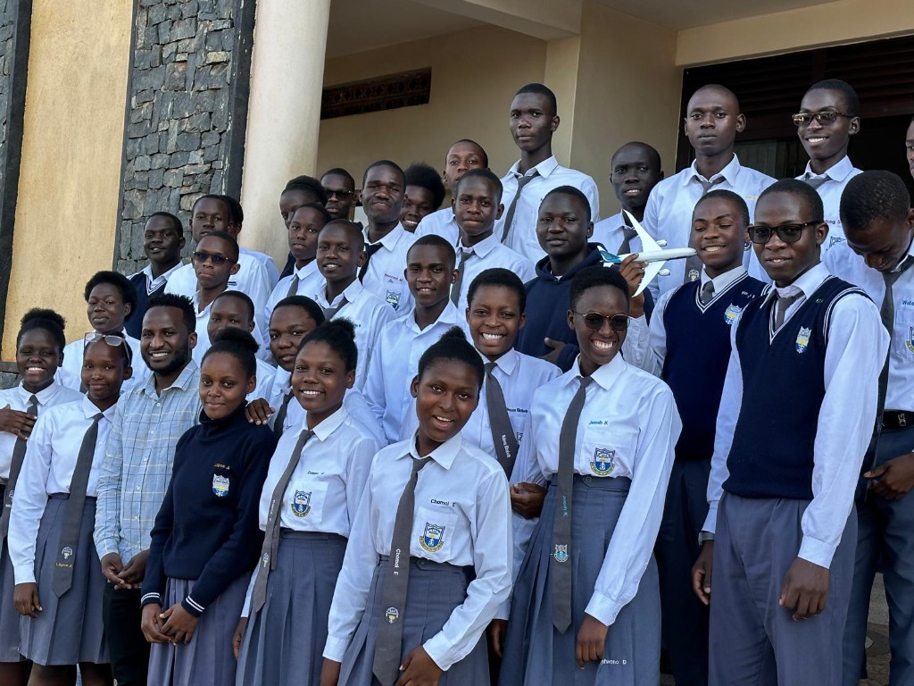 Large group of students in school uniforms smiling together on outdoor steps, one holding a small model airplane